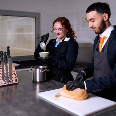 Twee studenten in de keuken scheppen soep in soepkom en snijden brood
