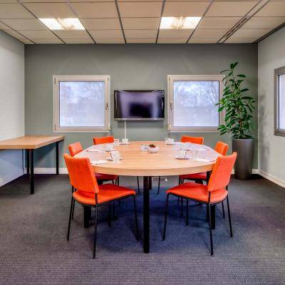 Kleine vergaderruimte met tafel rode stoelen scherm en ramen