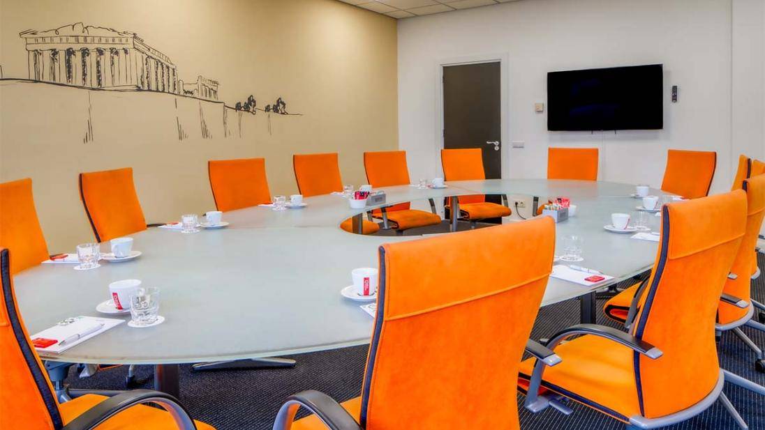 Vergaderruimte met oranje stoelen scherm en muurschildering