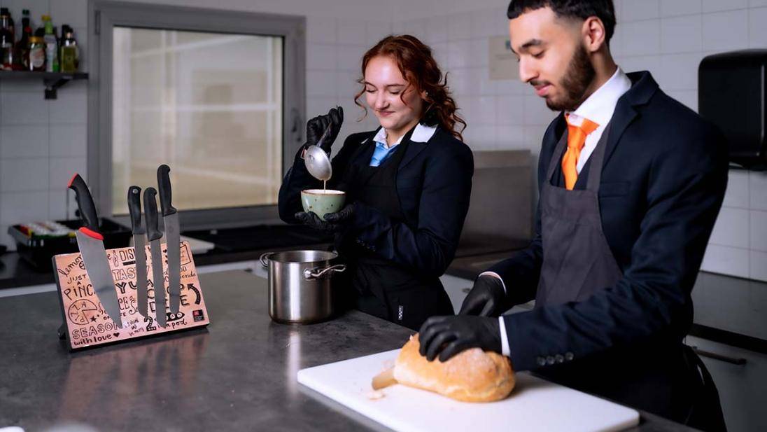 Twee studenten in de keuken scheppen soep in soepkom en snijden brood