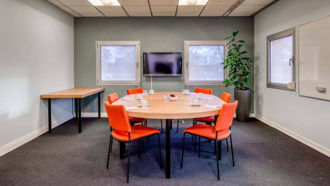 Kleine vergaderruimte met tafel rode stoelen scherm en ramen