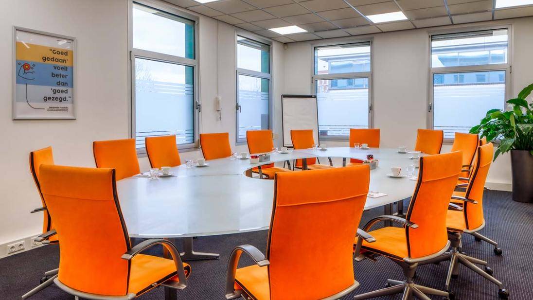 Grote vergaderruimte met oranje stoelen tafel en ramen